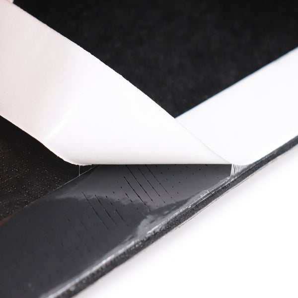 Nahaufnahme einer schwarzen, selbstklebenden Akustikplatte mit teilweise abgezogener Schutzfolie.