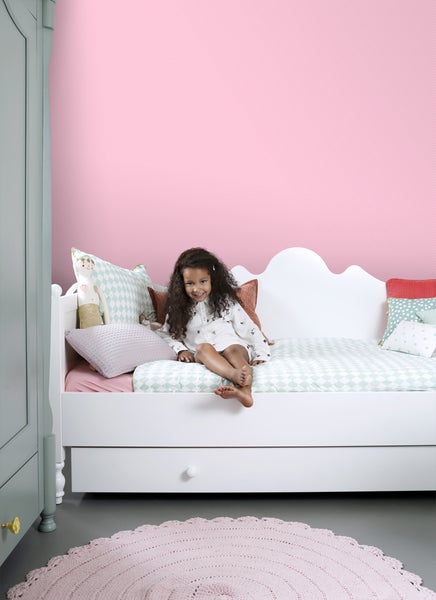 Kinderzimmer mit weißem Bett, gemusterten Kissen, Mädchen und rundem Teppich