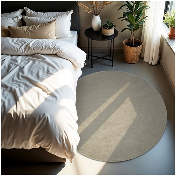 Runder beiger Teppich in einem hellen, modern eingerichteten Schlafzimmer neben einem Bett mit weißer Bettwäsche und Zimmerpflanzen.