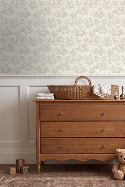 Vliestapete mit Toile-de-Jouy-Muster in einem hellen Kinderzimmer über einer weißen Wandvertäfelung und einer hölzernen Kommode.