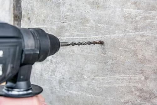 Eine Schlagbohrmaschine bohrt mit einem Steinbohrer ein Loch in eine Betonwand.