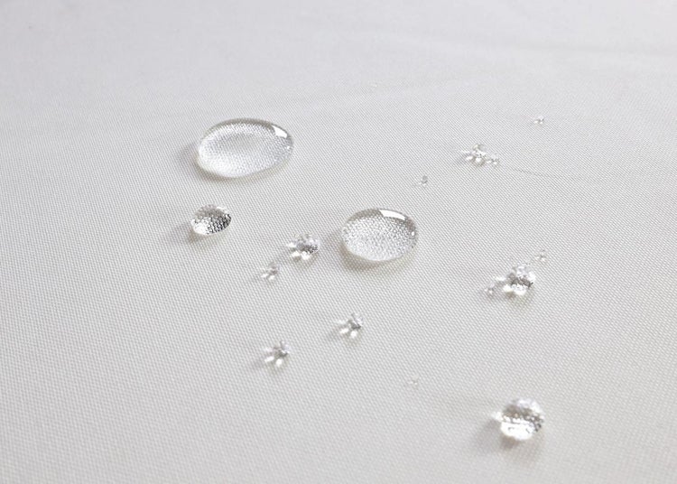 Nahaufnahme eines wasserabweisenden Stoffes mit abperlenden Wassertropfen auf der Oberfläche.