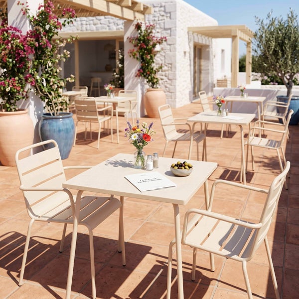 Helle mediterrane Terrasse mit quadratischen Bistrotischen und Gartenstühlen aus Metall auf Terrakotta-Fliesen.