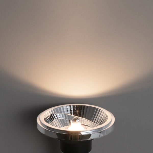 Silberne Reflektorlampe mit eingeschaltetem Lichtstrahl an einer Wand.