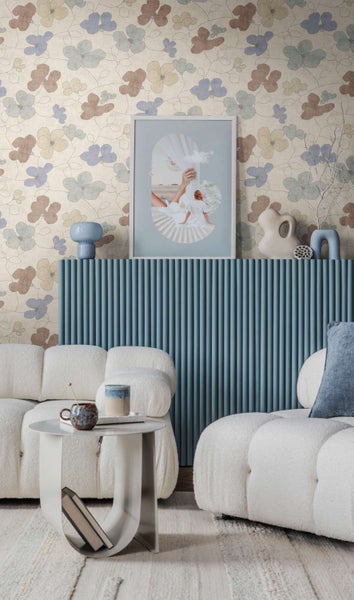 Wohnzimmer mit geblümter Tapete, blauem Lamellenmöbel, zwei Sofas in Teddyoptik und einem modernen Beistelltisch vor einem beigen Teppich.