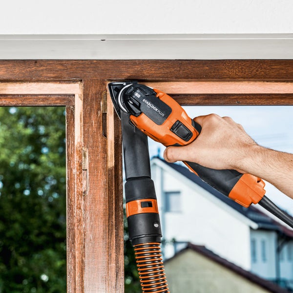Eine Person bearbeitet einen Fensterrahmen mit einem Multifunktionswerkzeug mit Staubabsaugung.
