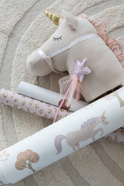 Dekorative Szene mit einem Steckenpferd-Einhorn, einem Zauberstab und verschiedenen Tapetenrollen mit kindgerechten Designs