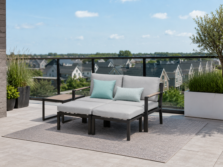 Modernes Gartenlounge-Set auf einer Dachterrasse mit Zweisitzer Sofa, zwei Hockern, Beistelltisch und grauen Polstern auf einem Outdoorteppich.