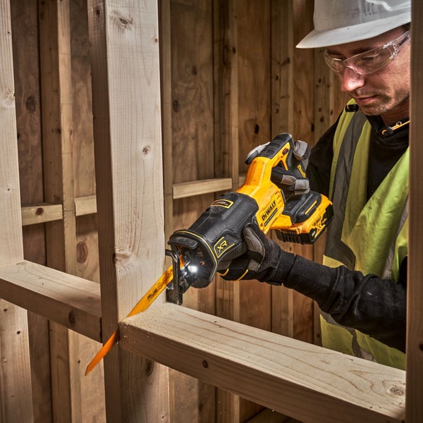 Handwerker mit Schutzausrüstung schneidet einen Holzbalken mit einer DeWALT Akku-Säbelsäge in einem Holzständerwerk.