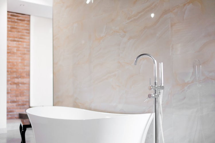 Badezimmer mit freistehender Badewanne und Armatur vor Marmorwand