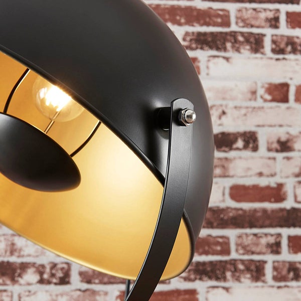 Detailaufnahme einer schwarzen Stehlampe mit goldener Innenseite vor einer Backsteinmauer