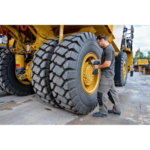 Ein Mann wechselt mit einem Akku-Schlagschrauber einen Reifen eines gelben Muldenkippers.