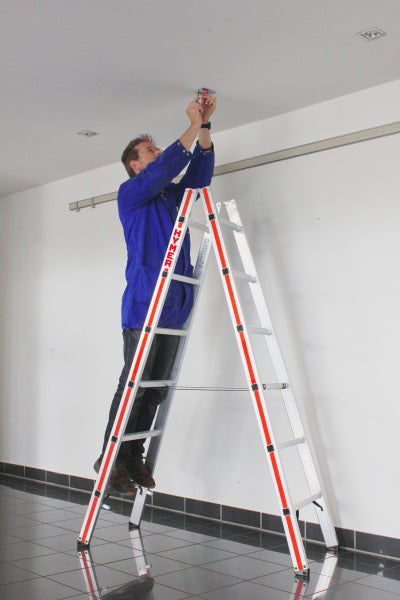 Mann auf einer Leiter, der an einer Deckenleuchte arbeitet.