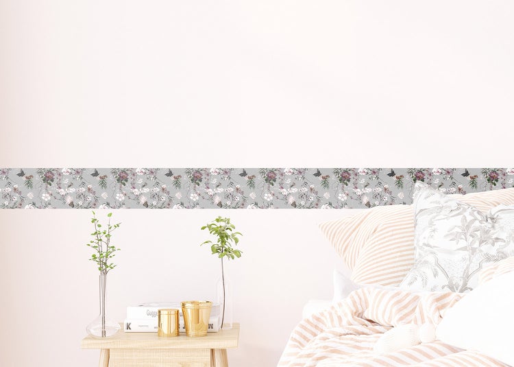 Selbstklebende Tapetenbordüre mit Blumenmuster und Schmetterlingen an einer weißen Wand in einem hellen Schlafzimmer.