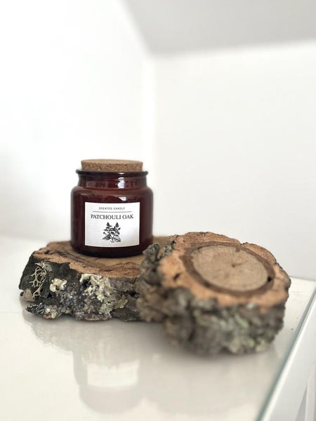 Duftkerze Patchouli Oak im Glas mit Korkdeckel auf einer Baumscheibe.