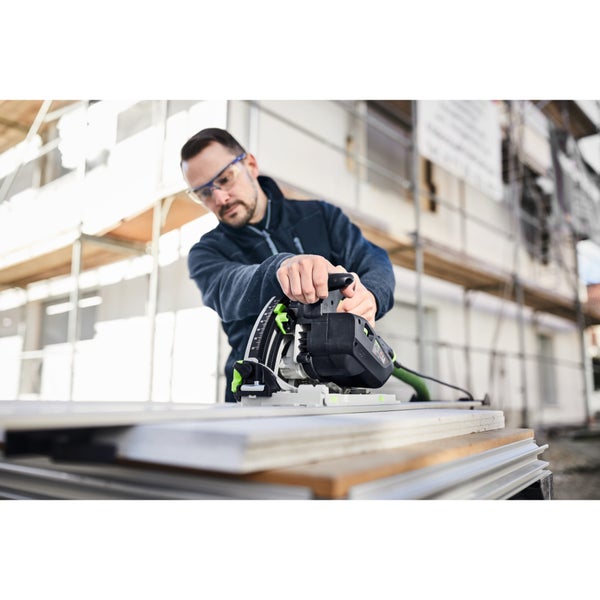 Handwerker bedient eine Tauchsäge auf einer Führungsschiene auf einer Baustelle im Außenbereich.
