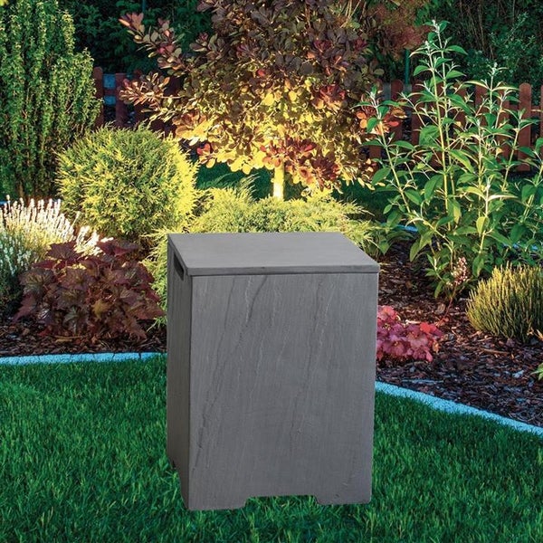 Quadratischer Gartenhocker in Steinoptik auf einer Rasenfläche in einem bepflanzten und beleuchteten Garten.