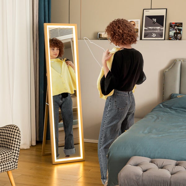 Ganzkörperspiegel mit LED-Beleuchtung und hellem Holzrahmen in einem Schlafzimmer, eine Person betrachtet sich im beleuchteten Spiegel.