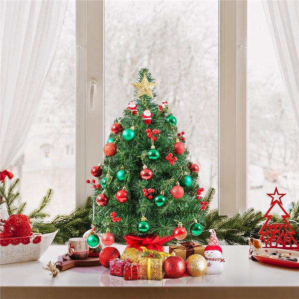 Dekorierter Weihnachtsbaum mit Christbaumkugeln, Geschenken und Dekoration vor einem Fenster.