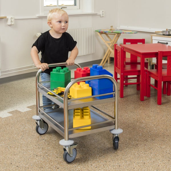 Kind schiebt einen Servierwagen mit Spielzeugbausteinen.