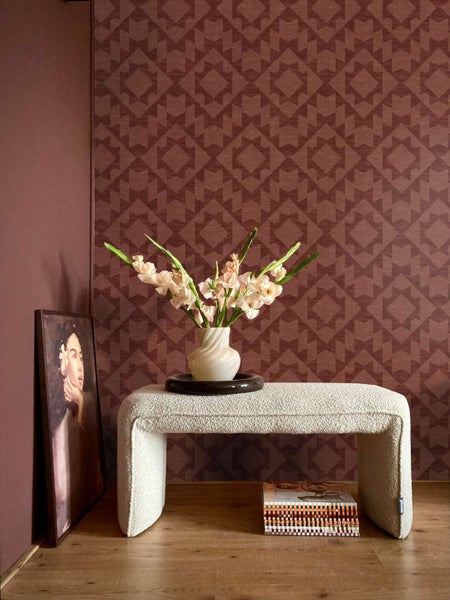 Wohnraum mit gemusterter Vliestapete, weißer Boucle Sitzbank, Vase mit Blumen und Wandbild auf einem Holzboden.