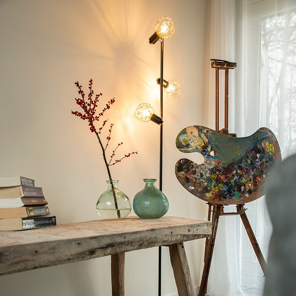 Stehleuchte mit drei Leuchten, Staffelei und Dekoration auf einem Tisch