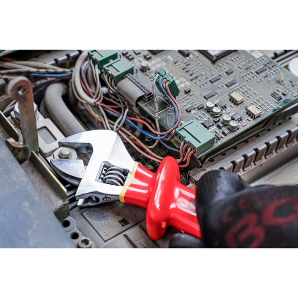 Hand mit Handschuh benutzt einen verstellbaren Schraubenschlüssel an einem elektronischen Gerät.