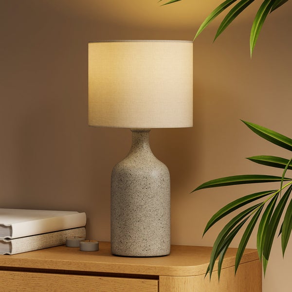 Dekorative Tischleuchte mit Lampenschirm auf einem Nachttisch mit Büchern und Kerzen