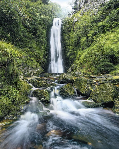 Wasserfall zwischen grünen Felsen und Vegetation