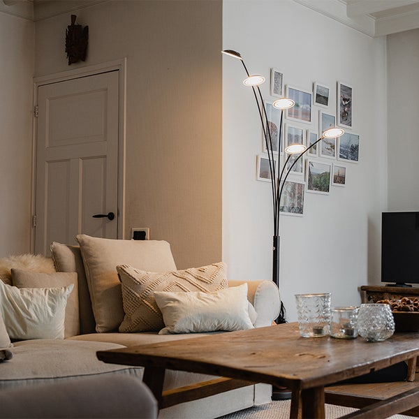 Wohnzimmer mit Sofa, Holztisch und Stehlampe mit mehreren Leuchten.