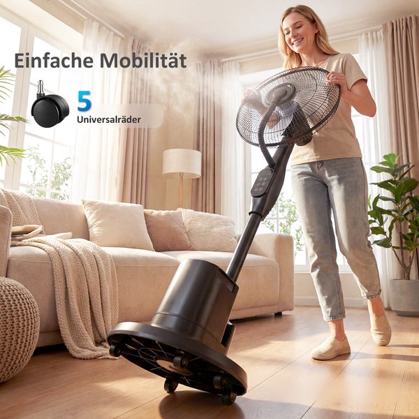 Eine Frau bewegt einen mobilen Sprühnebelventilator mit fünf Universalrädern in einem hellen Wohnzimmer mit Sofa und Pflanzen. Einfache Mobilität.