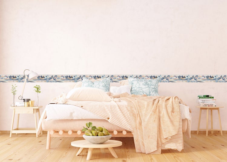 Helles Schlafzimmer mit Holzbett und einer Wandbordüre mit Gebirgsmotiv. Holztische und sanfte Farben sorgen für eine wohnliche Atmosphäre.