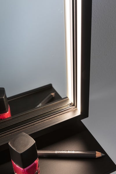 Detailaufnahme eines Spiegels mit LED-Lichtleisten im schwarzen Rahmen, davor Nagellack und Schminkstift.