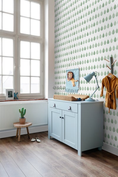 Hell und freundlich eingerichtetes Kinderzimmer mit Wickelkommode, Wanddekoration und Blattmuster-Tapete.