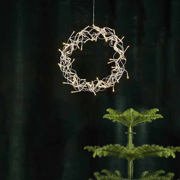 Dekorativer Leuchtkranz hängt über einem kleinen Weihnachtsbaum