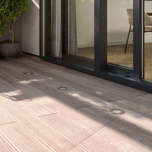 Terrassendielen aus Holz mit drei runden Bodeneinbauleuchten vor einer gläsernen Schiebetür.