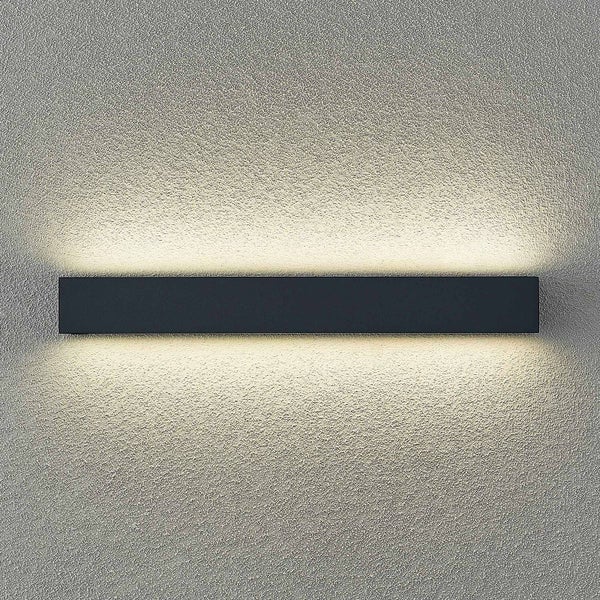 Schwarze rechteckige Wandleuchte mit Lichtaustritt nach oben und unten an einer strukturierten Wand.