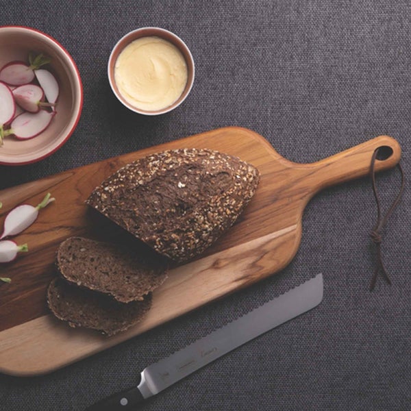 Brotlaib und Brotscheiben auf einem Holzbrett mit Radieschen, Butter und Brotmesser.