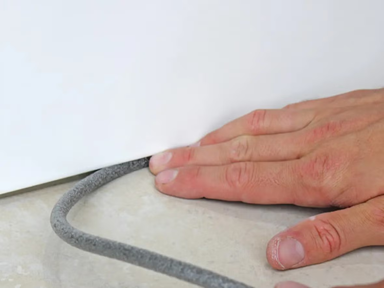 Hand drückt Fugenschnur in Spalt zwischen Bodenbelag und Wand