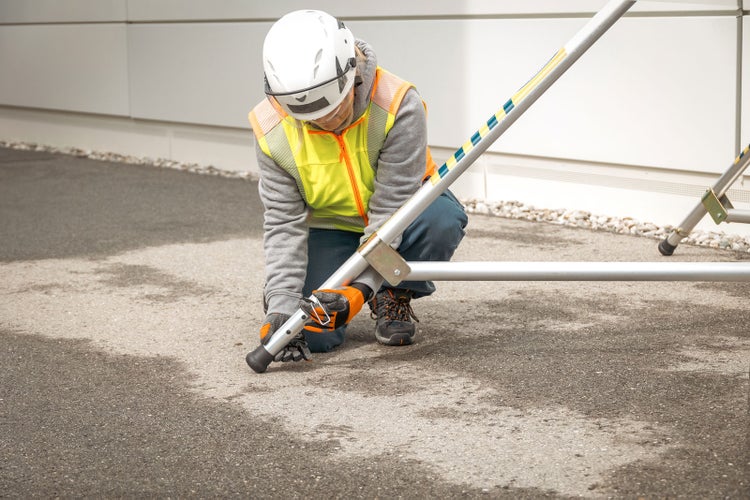 Eine Person mit Schutzhelm und Warnweste montiert ein Baugerüst.