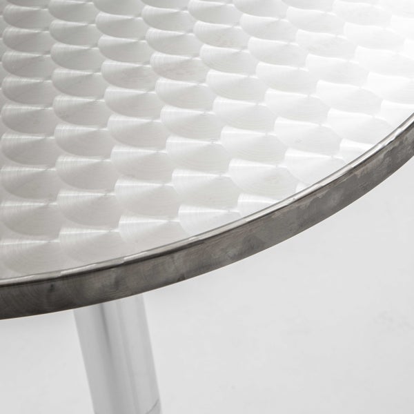 Nahaufnahme eines runden Bistrotischs mit gebürsteter Aluminiumoberfläche und dekorativem Kreismuster.