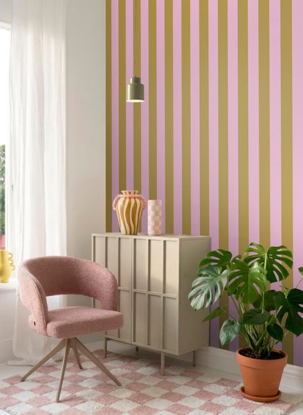 Gestreifte Tapete mit vertikalen Streifen in Rosa und Gold in einem hellen Wohnraum mit Sideboard und Sessel.