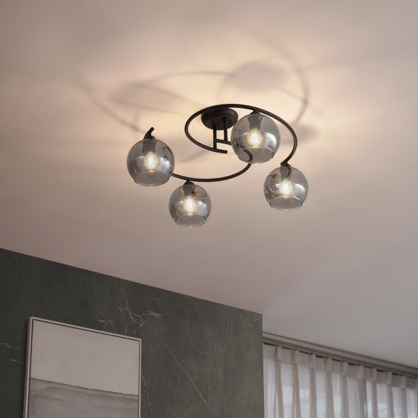 Moderne Deckenleuchte mit schwarzem Metallgestell und vier kugelförmigen Glasschirmen in Rauchglasoptik an einer hellen Decke.