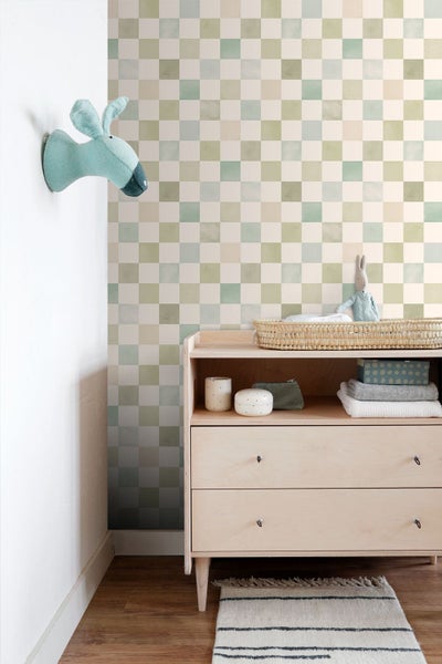 Kinderzimmer mit karierter Tapete in Grün- und Beigetönen, einer Wickelkommode aus hellem Holz und Wanddekoration.