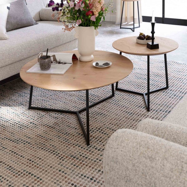 Set aus zwei runden Couchtischen mit Holzplatte und schwarzem Metallgestell auf einem gemusterten Teppich im hellen Wohnzimmer.