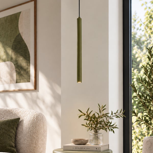 Moderne zylindrische Pendelleuchte in einem Wohnzimmer neben einem Fenster mit dekorativen Pflanzen und einem Sofa.