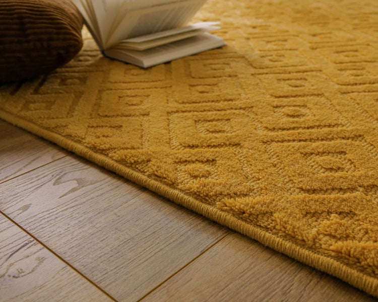 Helles, organisiertes Wohnzimmer mit gelbem Teppich mit Rautenmuster, Sofa, Holzkommode und Holzboden.