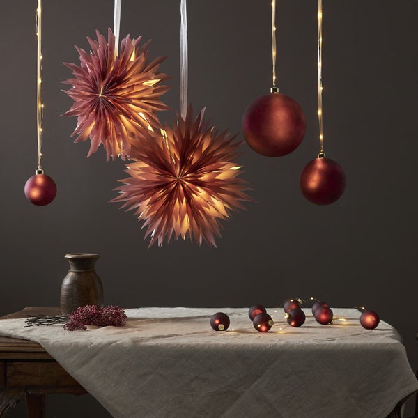 Festliche Dekoration mit Papiersternen, Weihnachtskugeln und Lichterketten auf einem Tisch