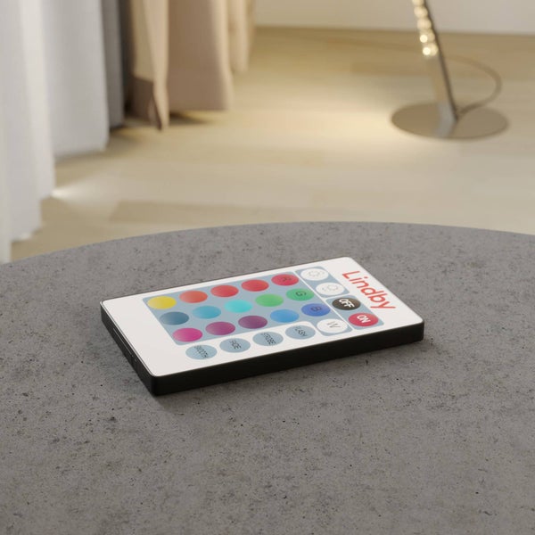 Lindby Fernbedienung für LED-Leuchten mit Lindby Logo und farbigen Tasten auf grauer Oberfläche in einem hellen, modernen Raum.