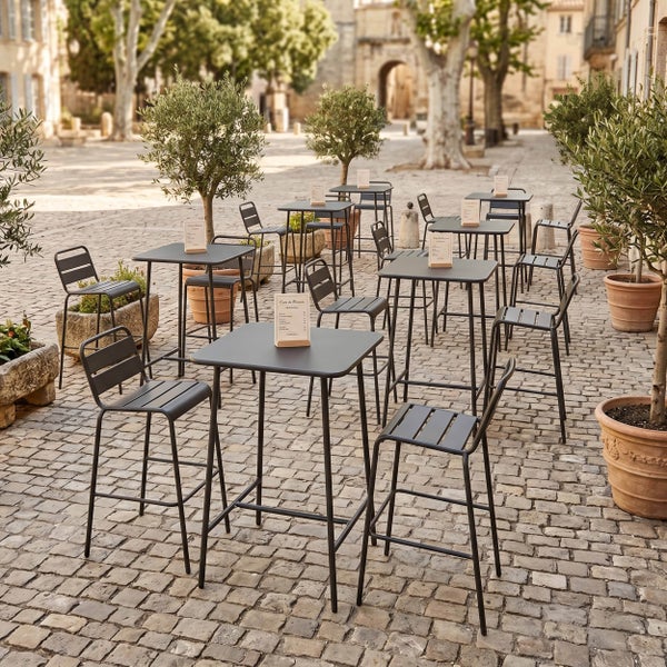 Schwarze Bar-Gartenmöbel-Sets aus Metall mit hohen Stehtischen und Barhockern auf einer gepflasterten Terrasse mit Olivenbäumen.